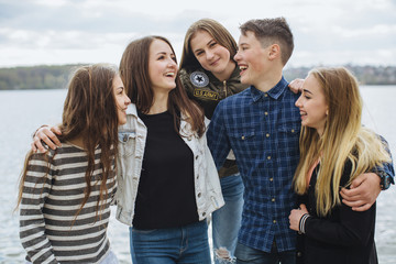 Summer holidays and teenage concept - group of smiling teenagers hanging outside near lake.