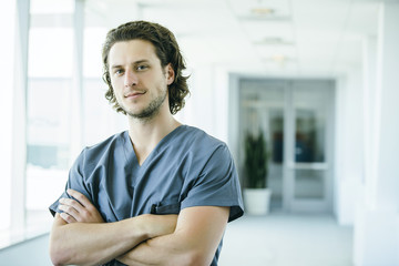 Portrait of confident, happy male nurse in hospital hallway
