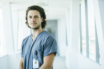 Portrait of confident, happy male nurse in hospital hallway