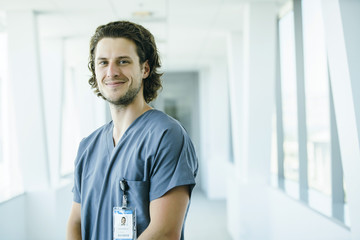 Portrait of confident, happy male nurse in hospital hallway