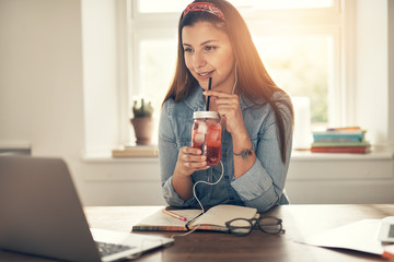Smiling businesswoman at laptop with drinking jar