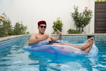 Young strong man drinking beer on an air bed in the pool. 