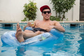 Young strong man drinking beer on an air bed in the pool. 