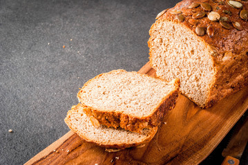 Freshly baked homemade organic multi-grain bread with pumpkin seeds on a cutting board on a black stone table. Copy space
