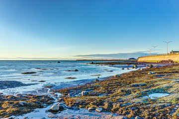 Sunset in Rimouski, Quebec by Saint Lawrence river in Gaspesie region of Canada with rock boulders in shallow water with pier