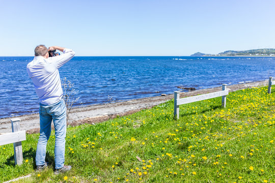 Young fit man photographer taking pictures of Gaspesie coast in Capucins, Quebec, Canada with Saint Lawrence river
