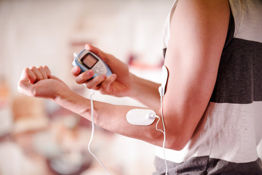 Close-up of a man holding an electrode machine in his hand and with electrostimulator electrodes in the arm of a fitness young man in a blurred background