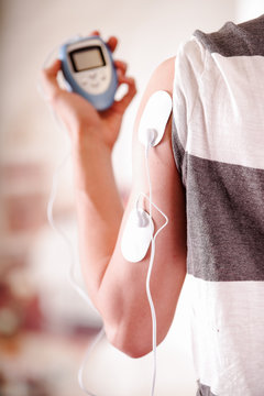 Close-up of a man holding an electrode machine in his hand and with electrostimulator electrodes in the arm of a fitness young man giving a back in a blurred background