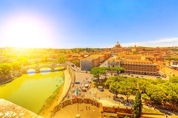 Fototapeta na wymiar aerial view at sunset of Vittorio Emanuele II Bridge and Tevere river from overlook of Castel Sant'Angelo castle in Rome city, Italy. Saint Peter basilica on background and italian flag waving.