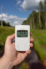 Geiger counter, radiation dosimeter, in hand measuring radiation radiation on a forest clearing with peat puddles.