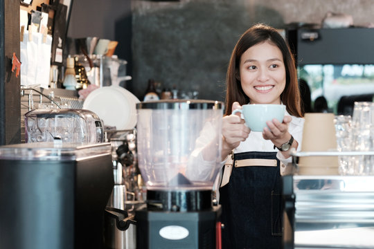 Young asian women Barista holding coffee cup with smiling face at cafe counter background, small business owner, food and drink industry