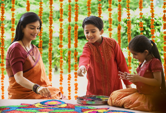Woman making a rangoli while her children watch 
