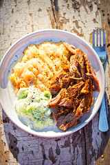 Pulled, seasoned pork, with mashed fried potatoes and cucumber and sour cream salad 