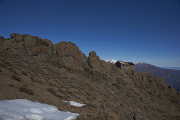 Derelict mountain hut, Refugio Alemana, in the mountainous landscape of Parque Yerba Loca set in a glacial valley close to Santiago, capital of Chile. Santiago in the distance under a layer of smog.
