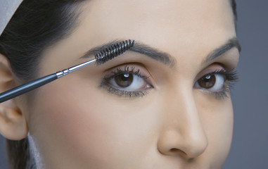 Close-up of young woman with eyebrow tinting applicator over colored background 