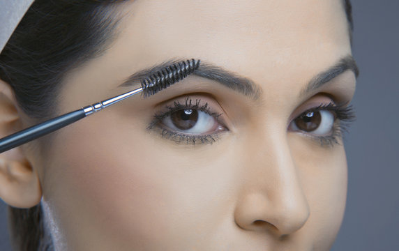Close-up of young woman with eyebrow tinting applicator over colored background 