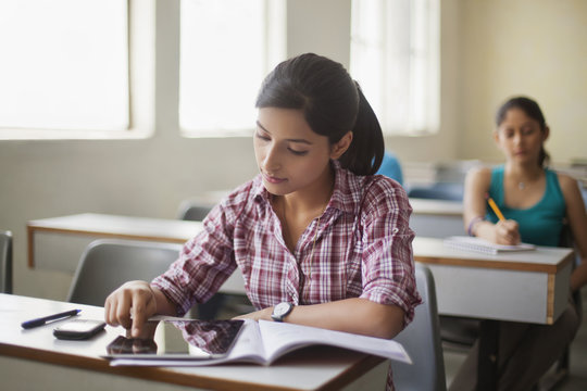 Teenage girl using digital tablet at desk in classroom