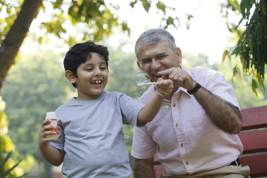 Boy blowing bubbles in a park while grandfather looks on