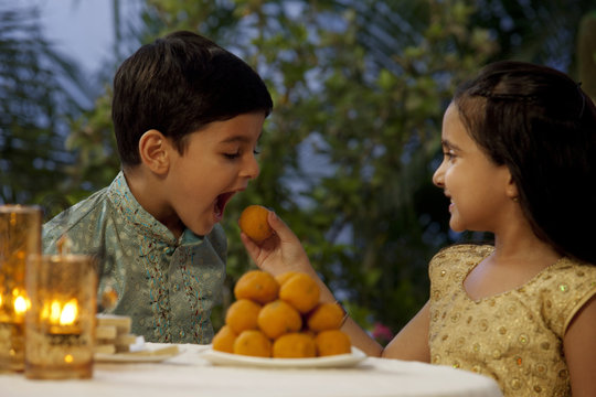 Girl feeding her brother a laddoo 