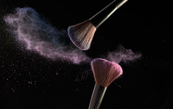 Make-up brushes with pink and blue powder explosion on black background