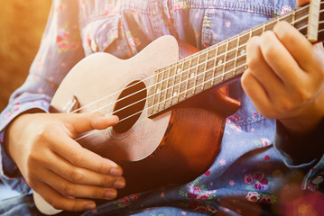 Obraz premium Close-up of little hipster girl playing ukulele guitar, vintage film tone effect
