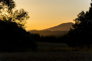 Dark nature during sunset. Silhouette of trees and hills under the orange sky. It is sundown.