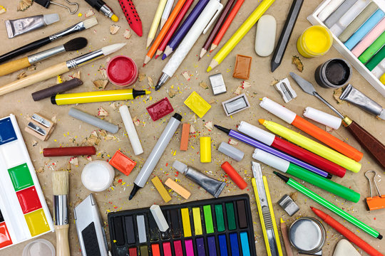 colorful school supplies on recycled paper background: watercolor, colored pencils and markers, chalks, various paintbrushes, sharpener