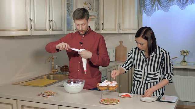 Young man and woman in the kitchen decorate with cream muffins