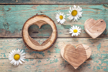 Wooden hearts with daisies on old turquoise wooden background.