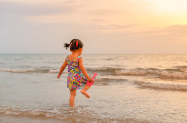 Fototapeta premium Soft focus of little asian girl in swimming suite holding plastic toy running in the sea alone at sunset time