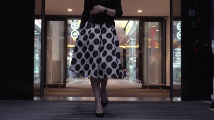 A beautiful woman in a dress comes out of the store through a sliding glass door