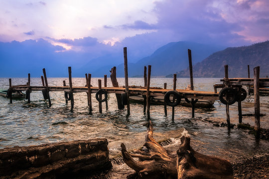 After sunset on Lake Atitlan viewed from the shores of Panajachel in Guatemala with an old rickety pier and some driftwood in the foreground.