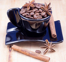Black cup filled with coffee beans, anise and cinnamon on wooden surface