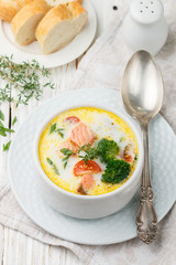 Salmon creamy soup with vegetables - potatoes, carrots, tomatoes and broccoli in a white bowl on bright wooden table