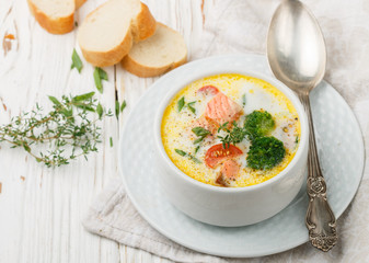 Chowder with salmon, potatoes, carrots, tomatoes and broccoli in a white bowl on bright wooden table
