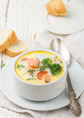 Chowder with trout and vegetables - potatoes, carrots, tomatoes and broccoli in a white bowl on bright wooden table