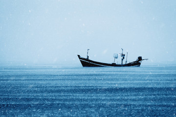 Fishing boat on the sea with snowfall in winter color tone.