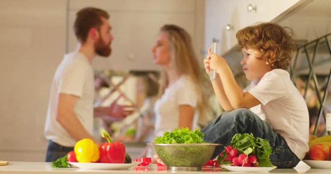 The background consisting of the emotional quarreling parents yelling at each other. The mother is slapping her husband in the front of the little child playing with his mobile phone.