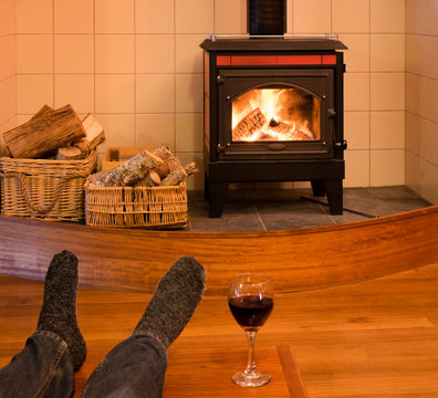 Feet with socks of a single man relaxing by fire in woodburning stove with glass of red wine - focus is on stove
