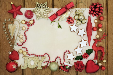Christmas background border with gold joy sign, gingerbread biscuits, bauble decorations, holly, mistletoe and foil wrapped chocolates  on parchment and oak wood.