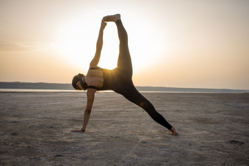 Fototapeta na wymiar Young fit woman training yoga poses in desert during the sunset or sunrise, female in black sportswear do stretching exercises 