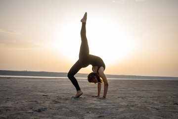 Young fit woman training yoga poses in desert during the sunset or sunrise, female in black sportswear do stretching exercises  