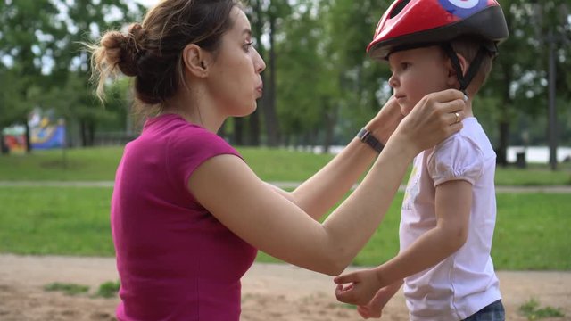 Mom helps his son put on a helmet to safely ride a bike in the city park