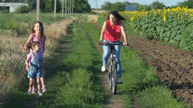 Children catch up with their mother riding a bicycle. Family in nature.