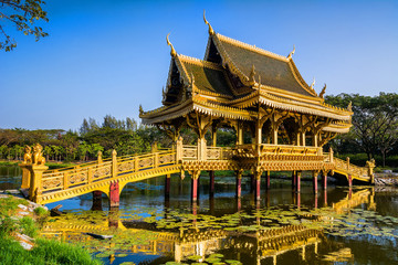 Fototapeta na wymiar Amazing view of beautiful Golden Bridge and Pavilion of the Enlightened with reflection in the water. Location: Ancient City Park, Muang Boran, Samut Prakan province, Bangkok, Thailand. 