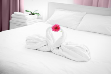 Two towel swans and flower on bed in hotel room