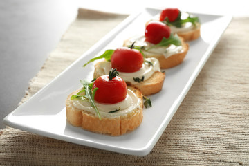Toasts with delicious cherry tomatoes, ruccola and sauce in platter on table