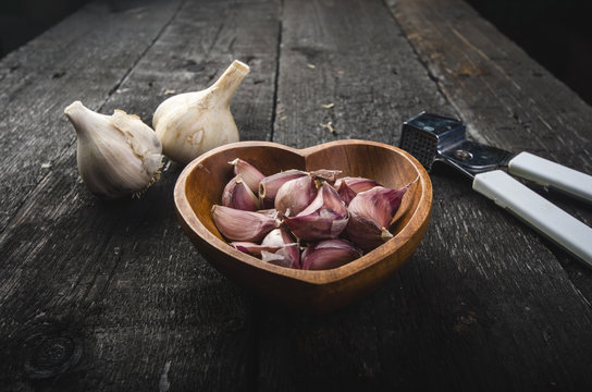 Cloves of garlic on a wooden black table. Fresh garlic bulb with iron garlic press. Vintage background.  Farmer. Medicine and healthy. Traditional medicine.