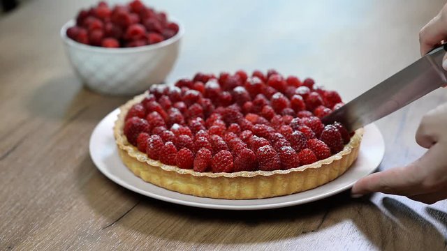 Woman's hand cut with a kitchen knife tart with raspberries