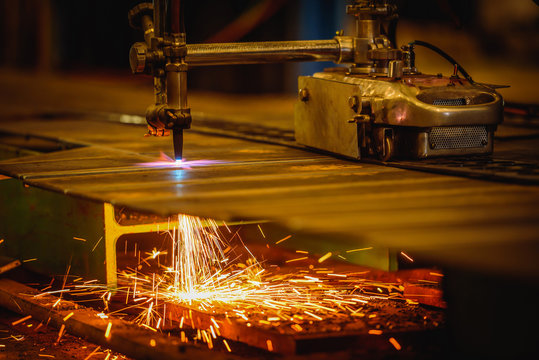 Worker cutting steel plate with acetylene welding cutting torch and bright sparks in factory